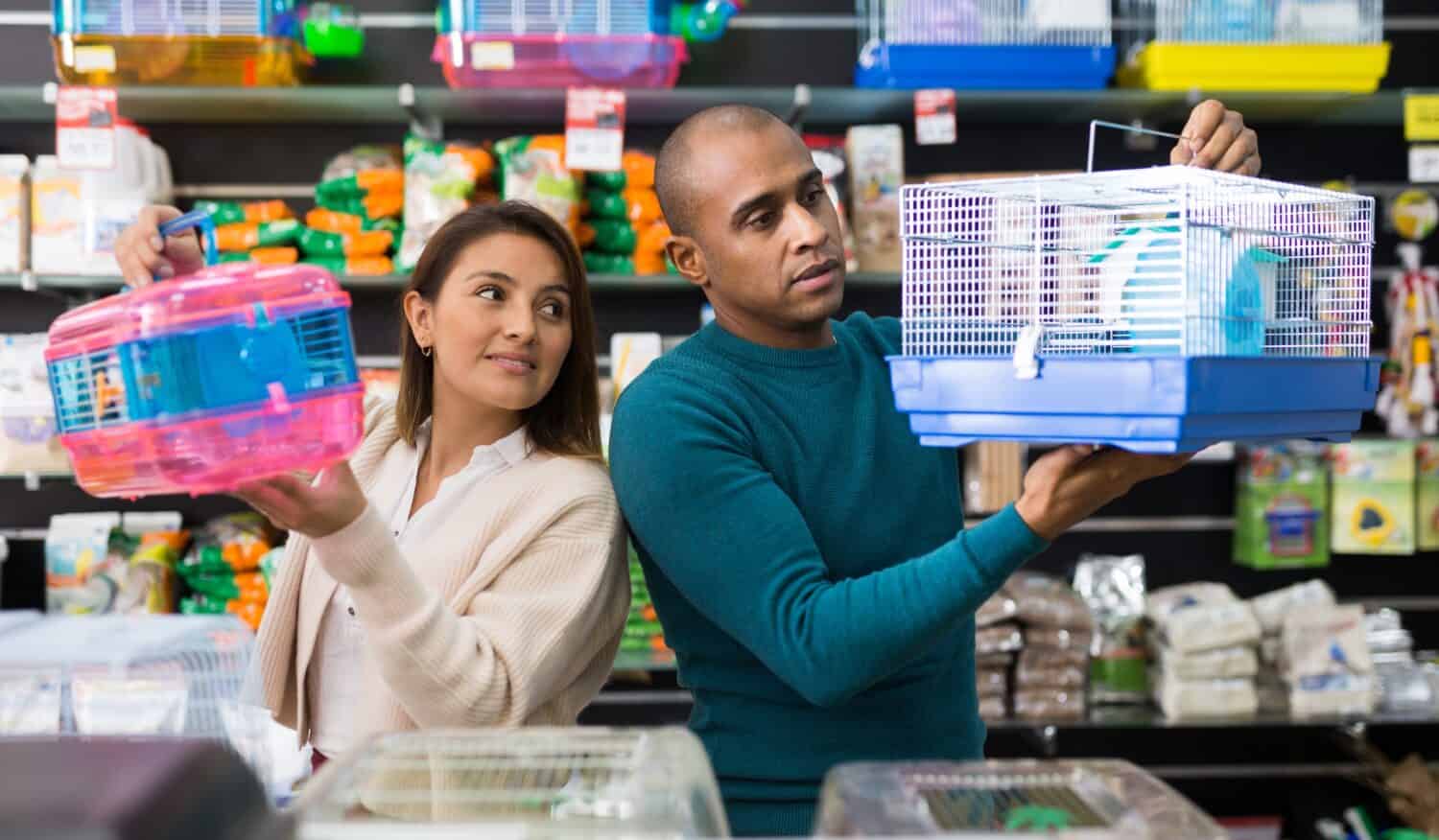 Man helping woman to choose hamster cage at pet store