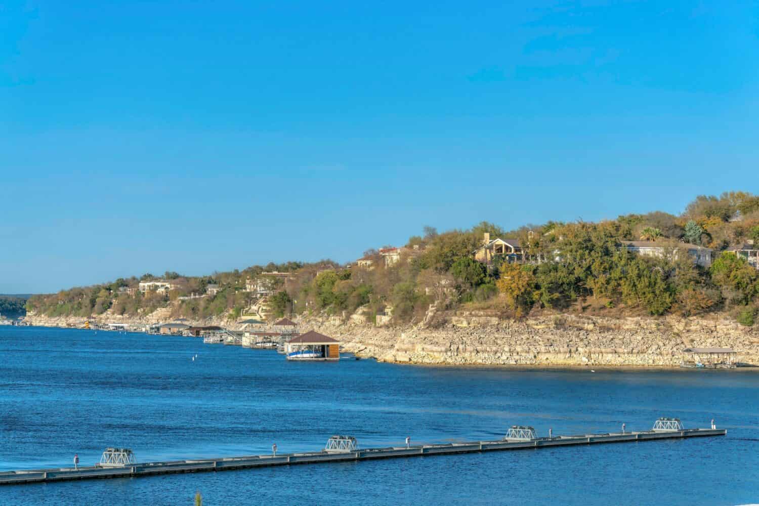 Lake Austin, Austin, Texas- Docks at the front of the rich neighborhood on top of the slope. There are large residential buildings on top with docks near the shore.