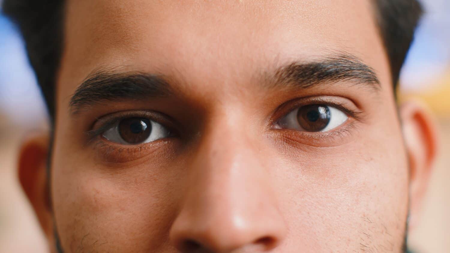 Extreme close-up macro portrait of smiling indian man face. Young guy eyes looking at camera. Adult positive hindu man opening wide his closed eyes. Brown eyes of brunette hispanic male attractive