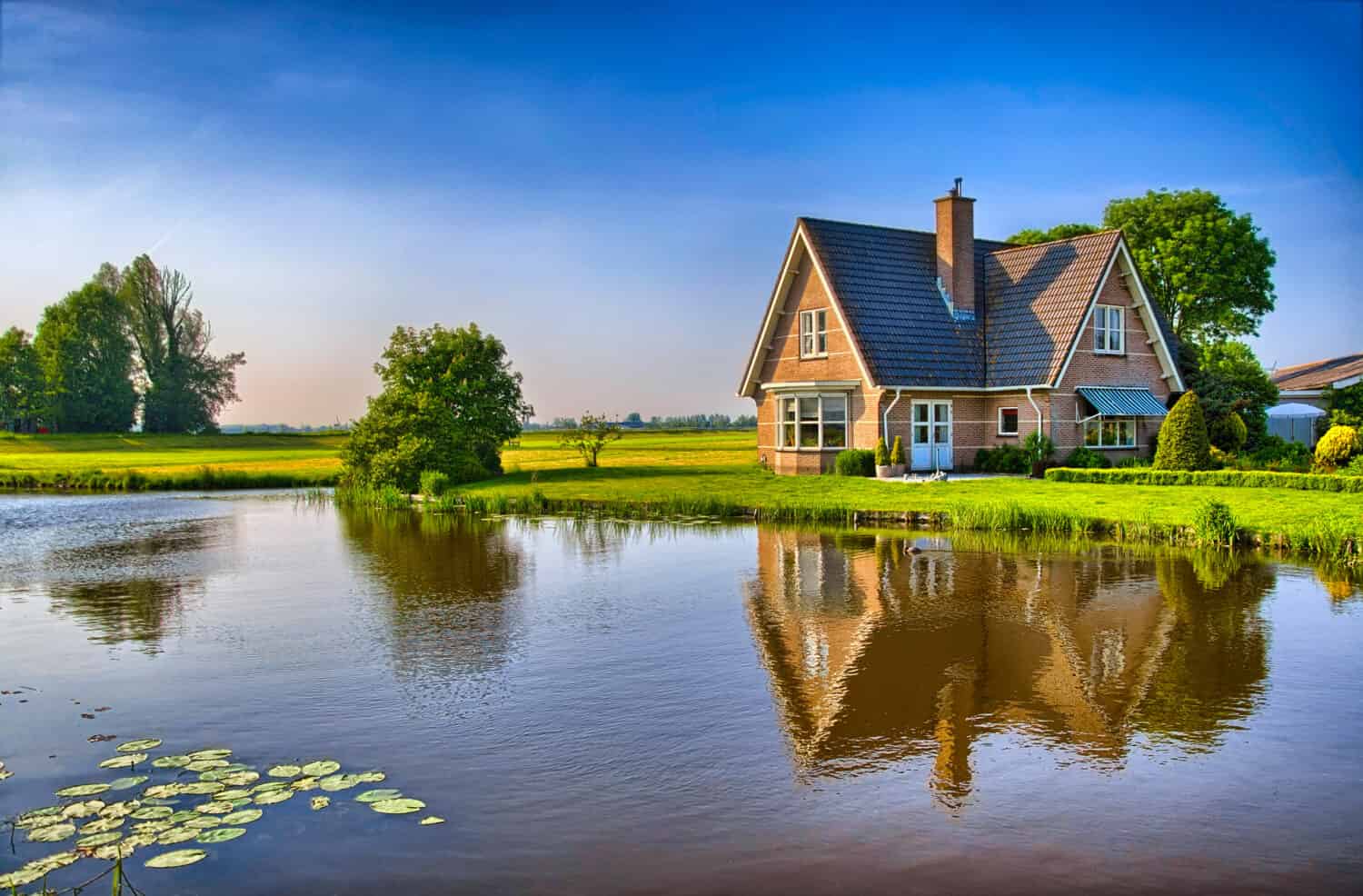 A red brick house sits in front of a lake. 