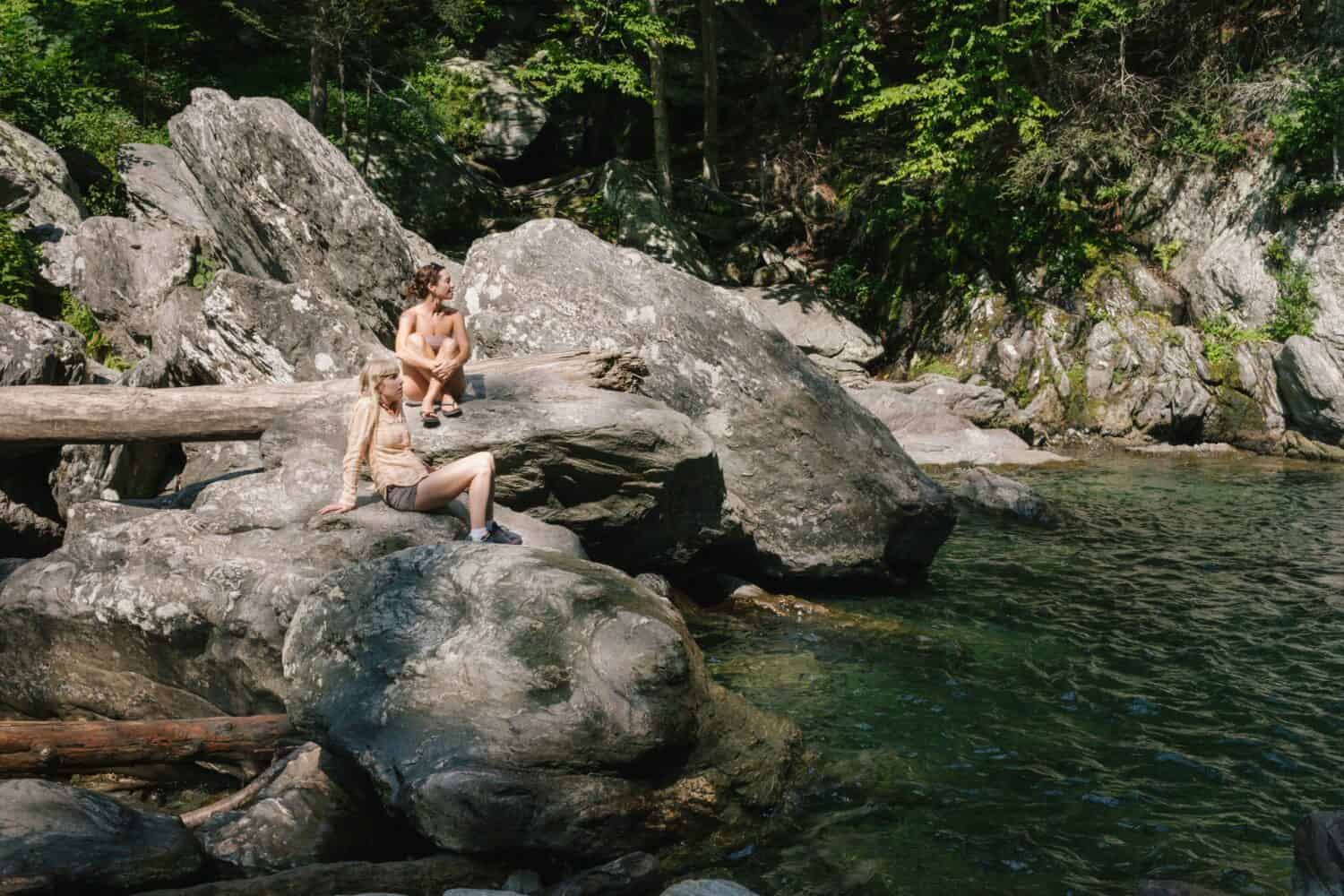 Two women sitting by a swimming hole in woods