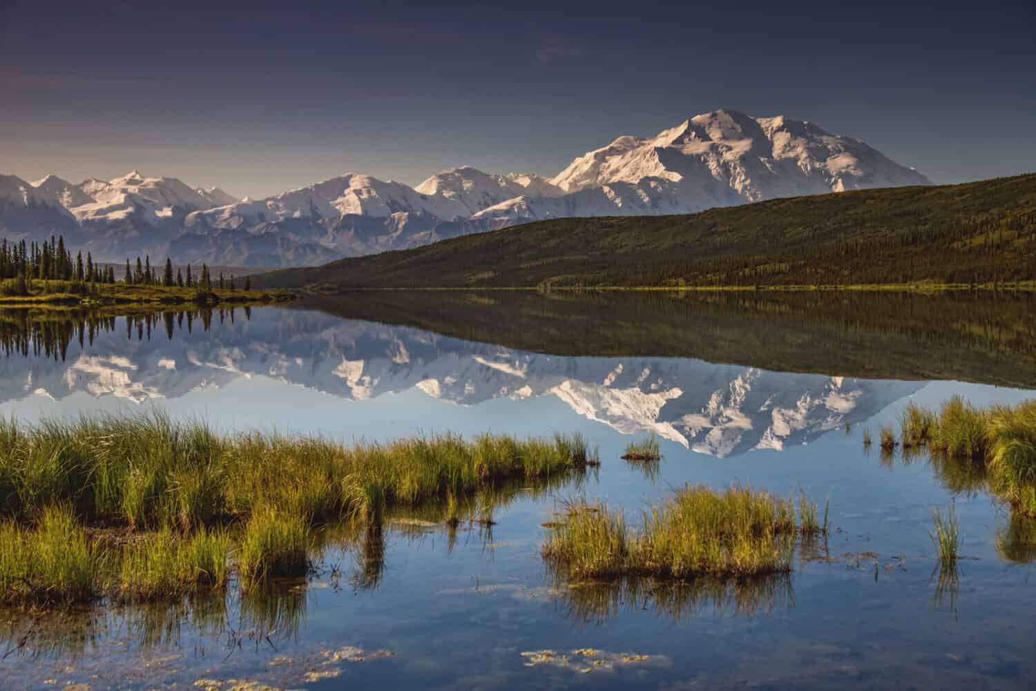 view of alaska's mount denali reflected in calm Wonder Lake, with clear blue sky above