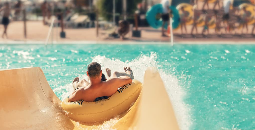 Cool people having fun on the water slide with friends and familiy in the aqua fun park glides playing happy and water splashes are all over. Blue sky background looks amazing sunlight