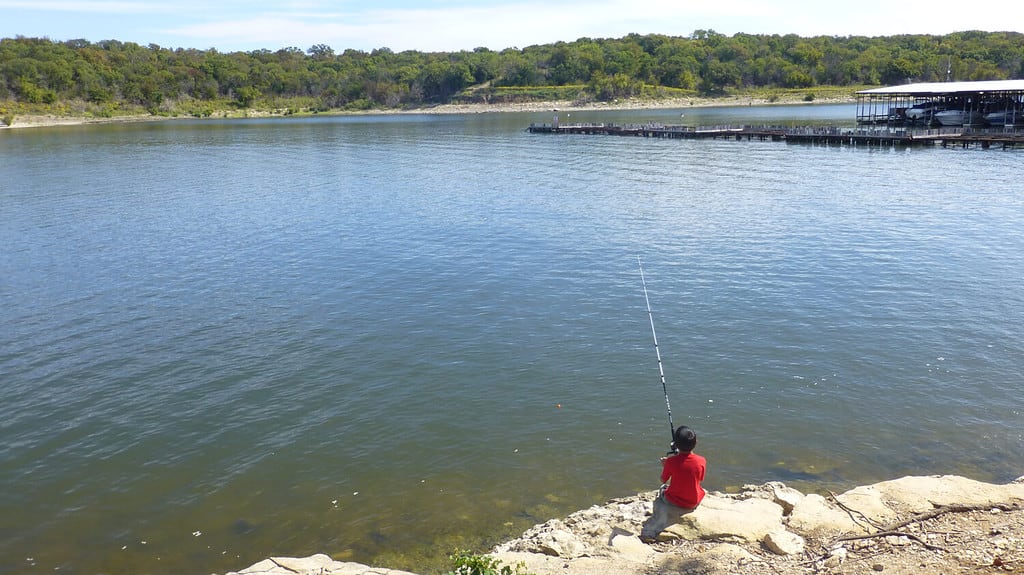 An angler seated casting a lure into the still waters of Hosmer Lake. 