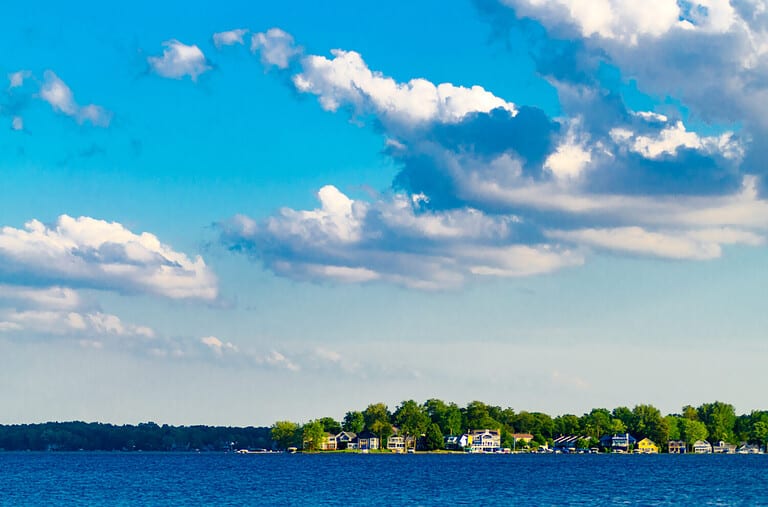 Vacation houses line the shores of Lake Maxinkuckee in Culver, Indiana, while white clouds drift against a blue sky