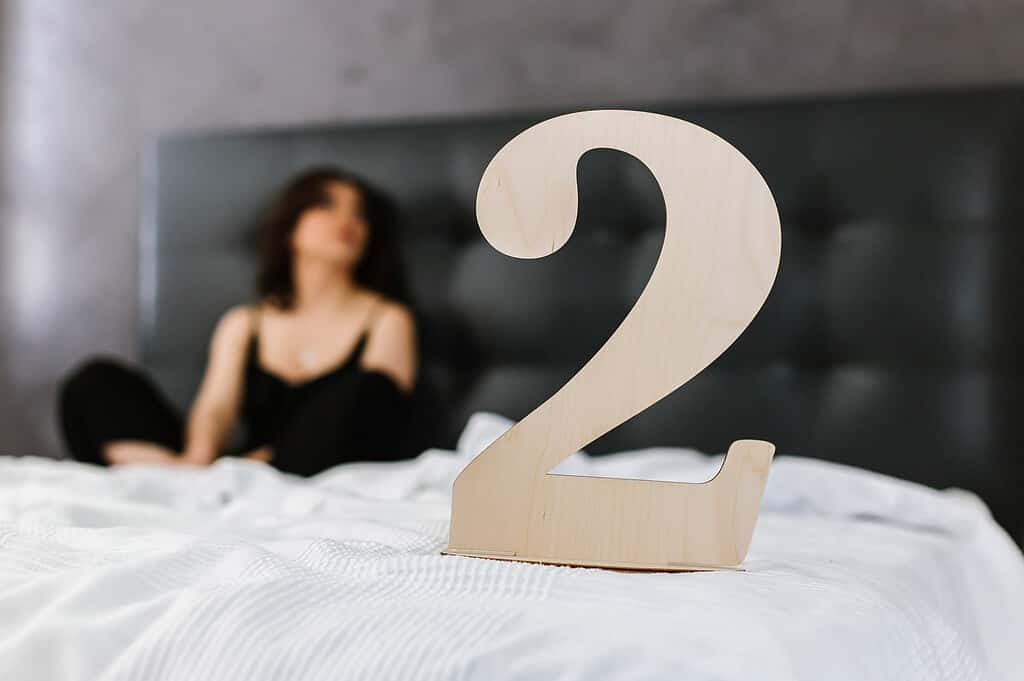 wooden plate with the inscription "two" stands on the bed, woman
