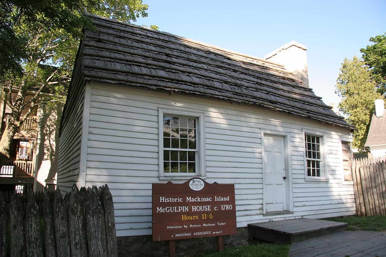 An old one story white house with a dark roof sits in front of a sign that reads, "Historic Mackinac Island — McGulpin House c. 1780."