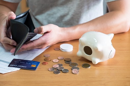 Selective focus at credit card and wallet. Men sit at the table while checking expense and credit card payment with blurred coin and empty piggy bank as the background. Personal financial problem.
