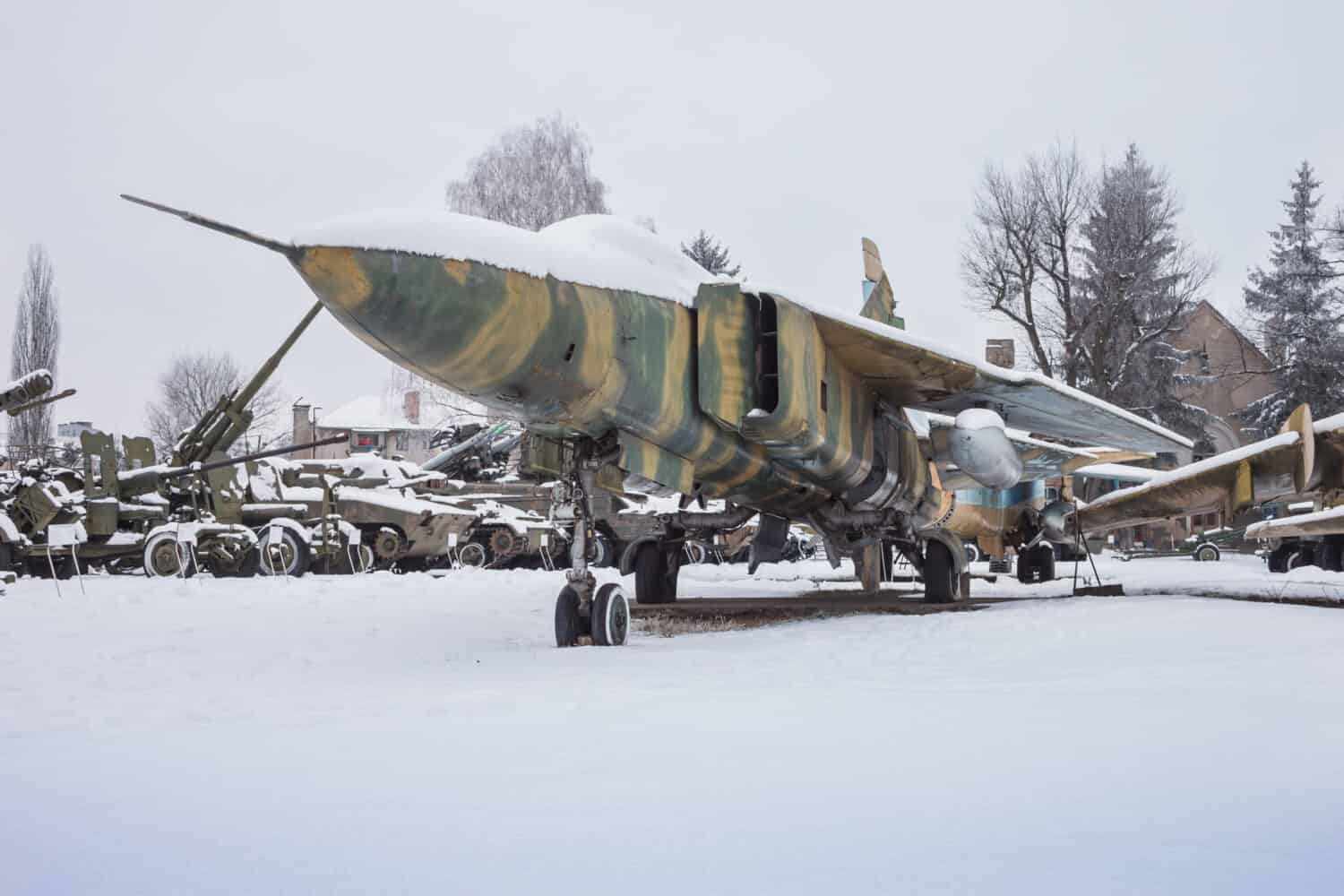 Old jet fighter is covered with snow on the background of military equipment
