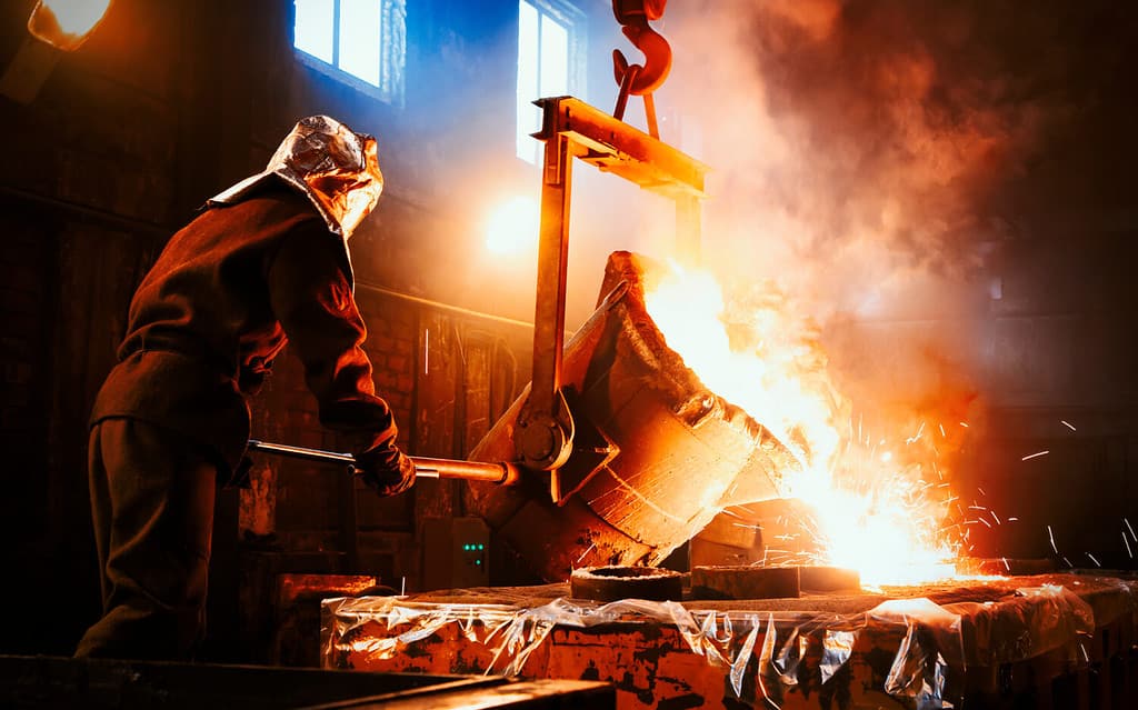 Workers operates at the metallurgical plant. The liquid metal is poured into molds. Worker controlling metal melting in furnaces.