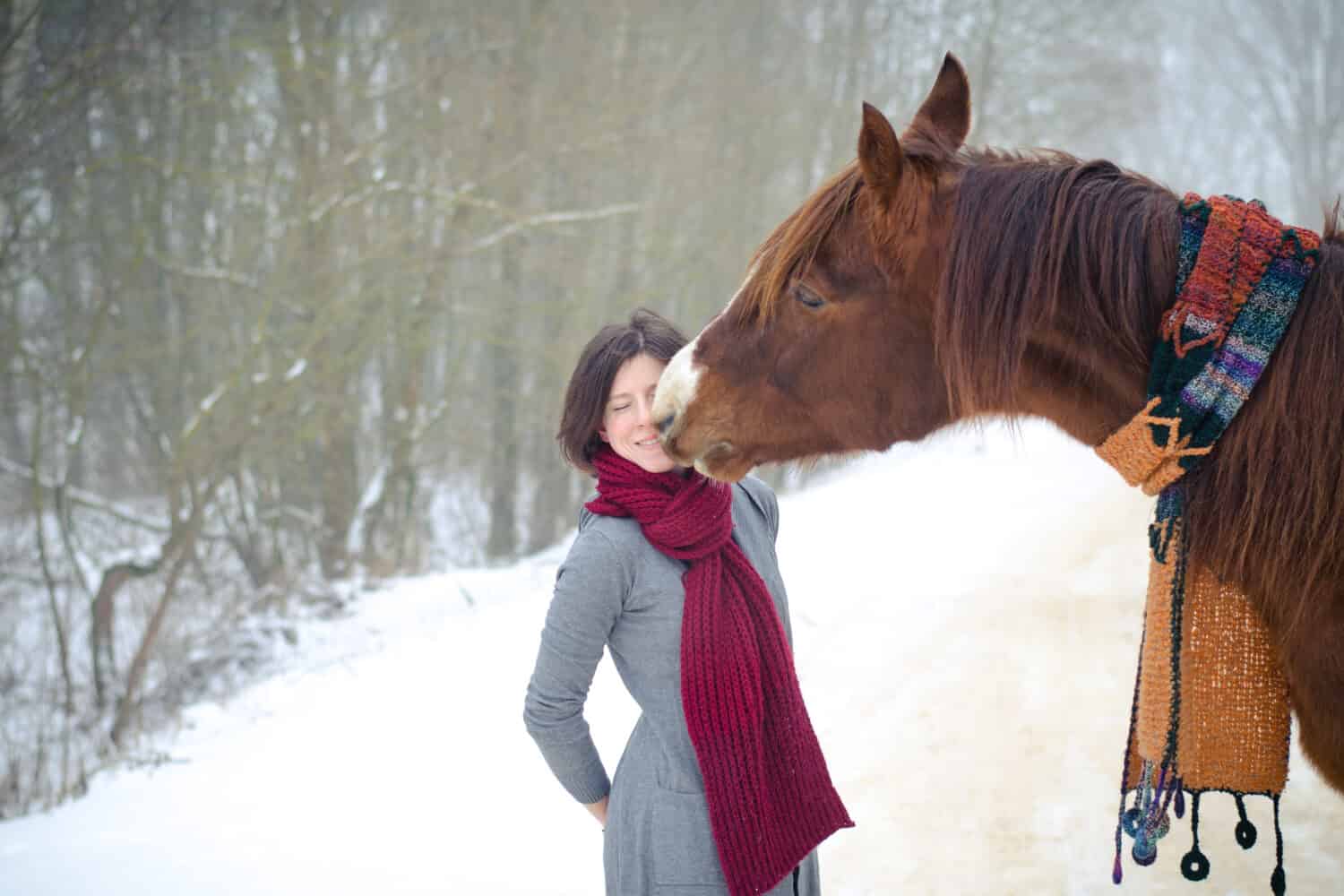 portrait of girl kissing red trakehner stallion horse with scarf in the winter
