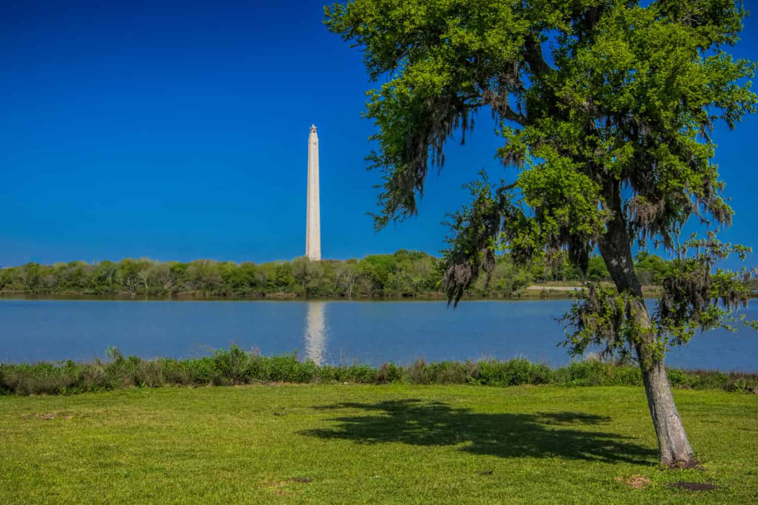 San Jacinto Monument under blue sky across from river.