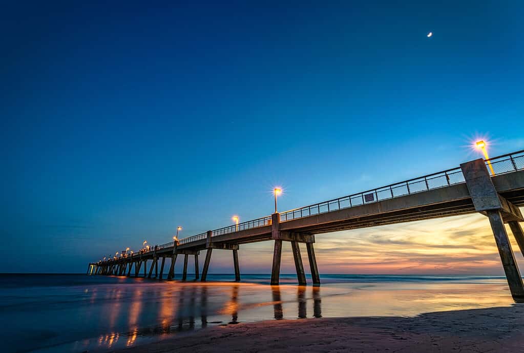 A fishing pier at night as the sun sets in the background and reflects off the ocean. This is a pier in Florida on Okaloosa Island, part of the Emerald Coast
