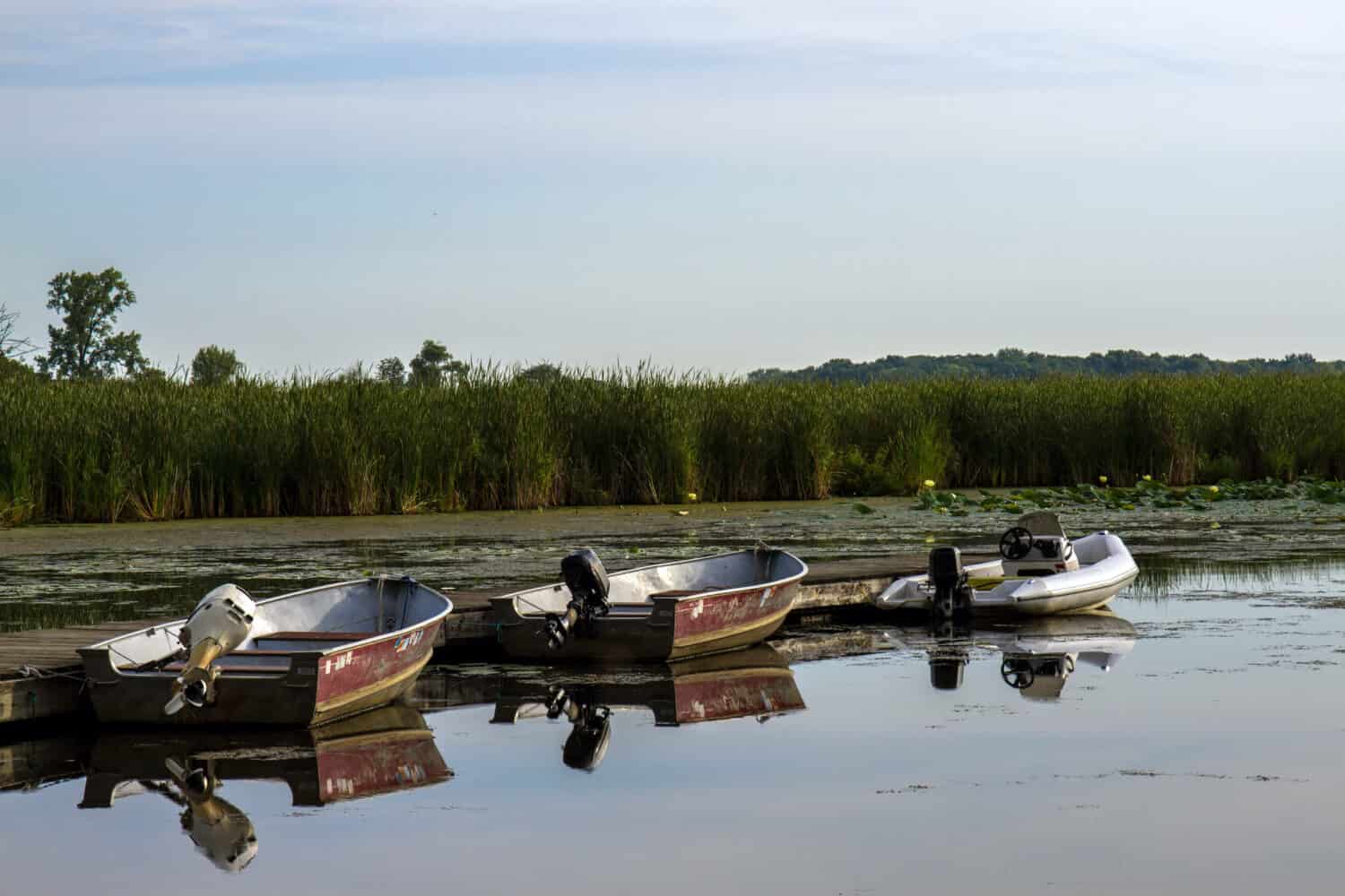 Three motorized fishing boats reflected in the water at dawn in Chain O' Lakes State Park near Antioch, Illinois