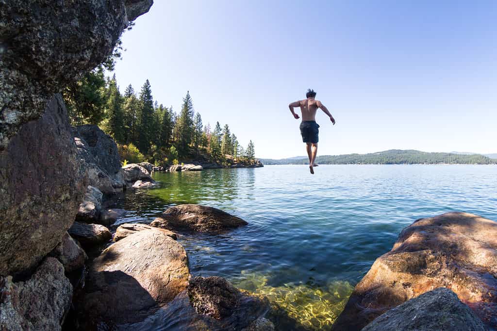 young man jumping of a rocky cliff in Tubs Hill in to Coeur d' Alene Lake in Northern Idaho