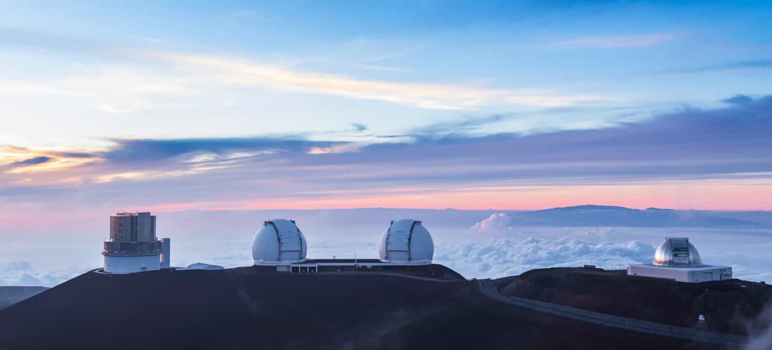 Above the main cloud layer, wispy clouds float between the observatories on Mauna Kea volcano, Hawaii, at sunset. Shown are Subaru Telescope, Keck I and II and NASA Infrared Telescope Facility.