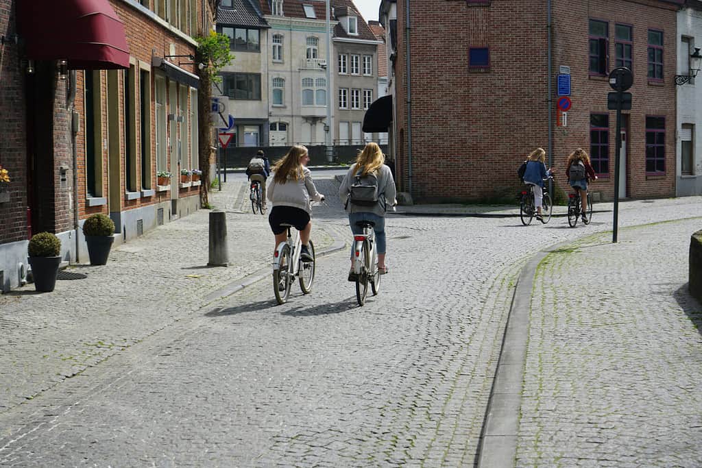 two women riding bicycles on european street. back of two cyclist. 2 girlfriends rides on an cobble stone on a bicycle on a background of building of hotel. City rent bike. Antwerp, Belgium.