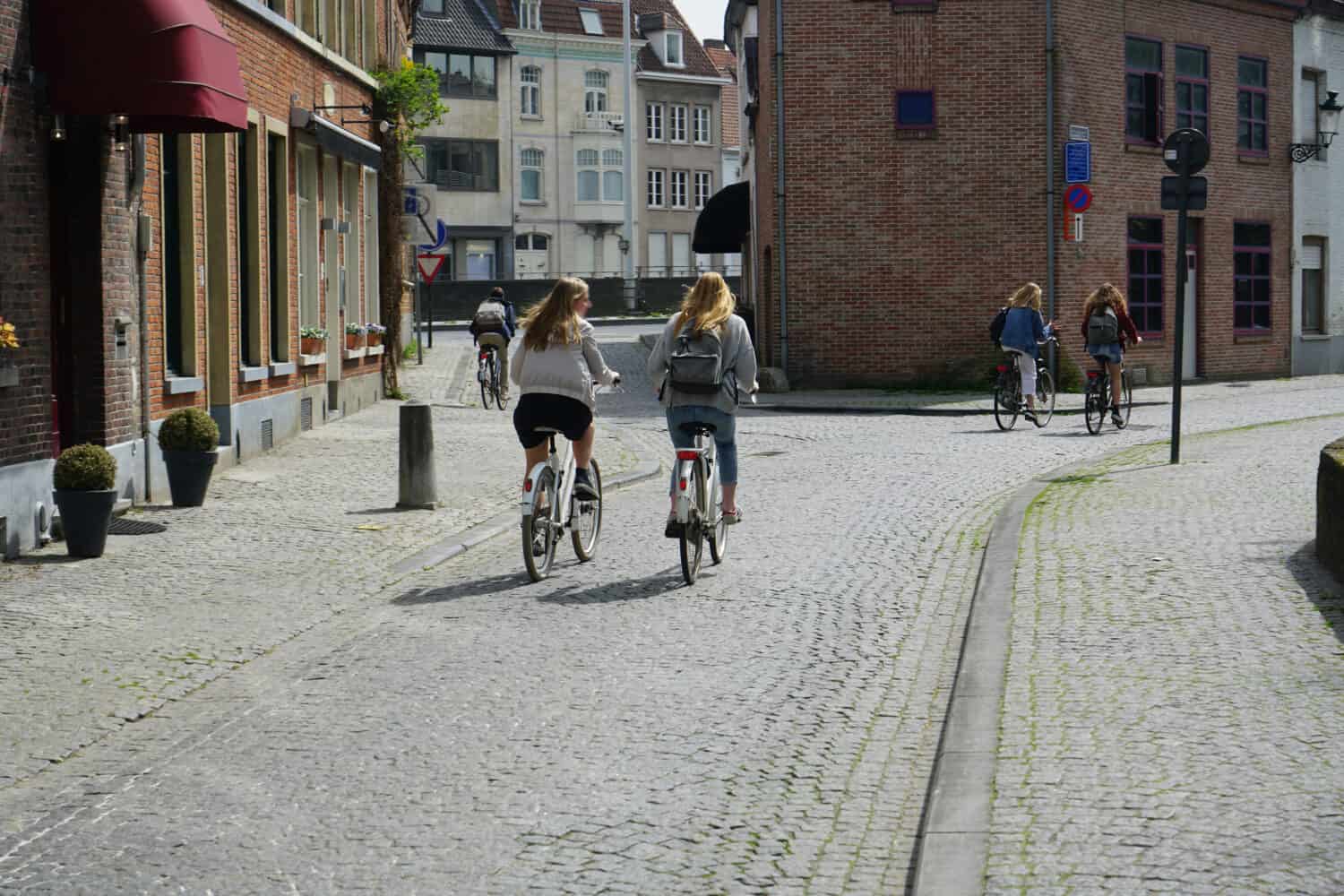 two women  riding bicycles on european street. back of two cyclist. 2 girlfriends rides on an cobble stone on a bicycle on a background of building of hotel. City rent bike. Antwerp, Belgium.