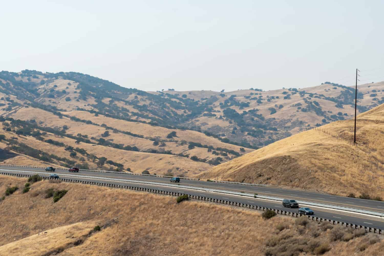 Freeway road with cars crossing the the San Luis Reservoir valleys during dry and hot season, San Luis Creek in the eastern slopes of the Diablo Range of Merced County, California. USA