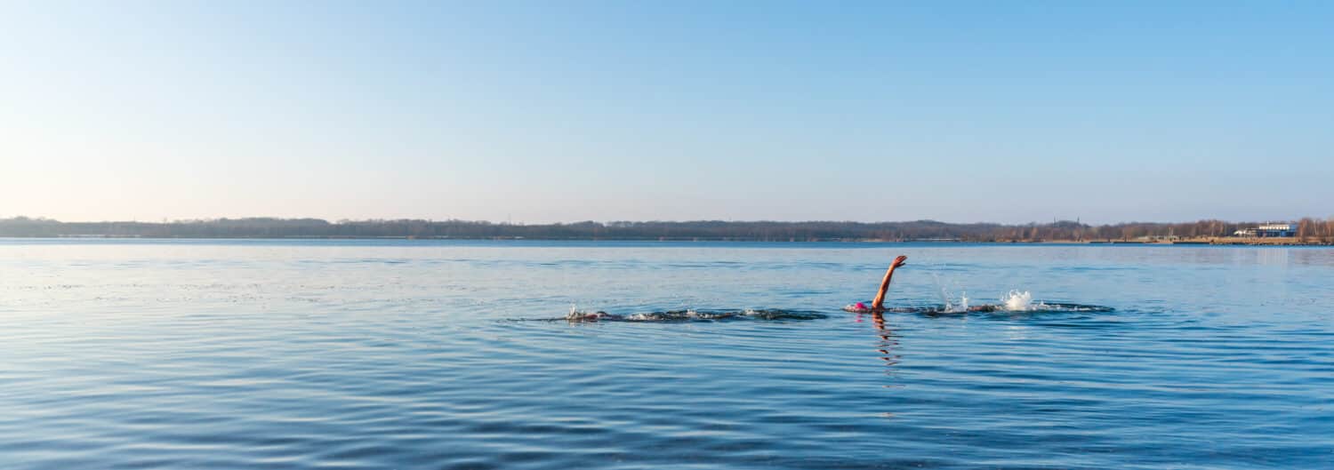 Two athletes swimming in a lake panorama
