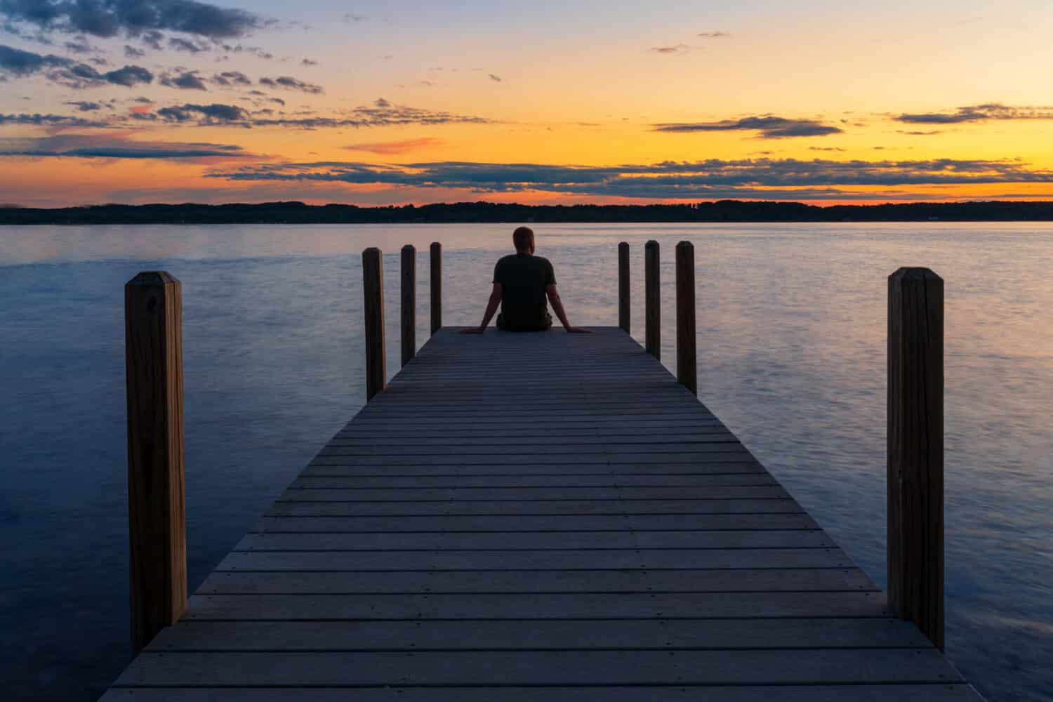 Person sitting on dock looking at sunset over lake.