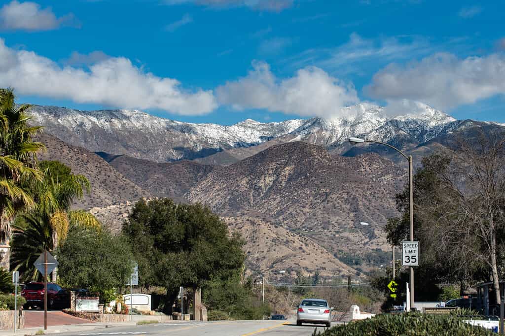 Chiefs Peak Mountain over Ojai, California is covered in snow and low clouds while overlooking highway 33 traveled by cars.