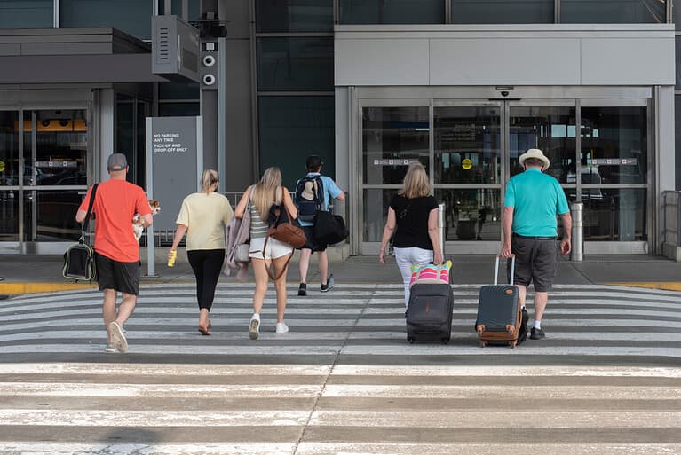 A group of passengers hauling luggage head towards the entrance of an airport terminal.