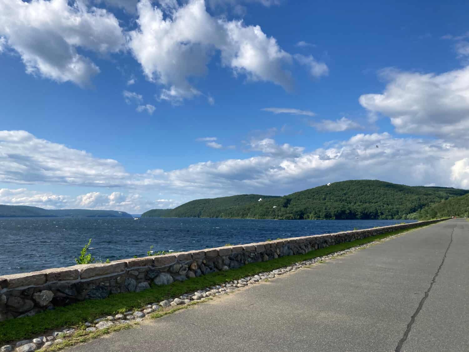 Beautiful summer day at the Quabbin Reservoir Windsor Dam with puffy clouds in the blue sky, rippling calm waves in the water, and a peaceful walkway lined with an old stone wall. Selective focus.