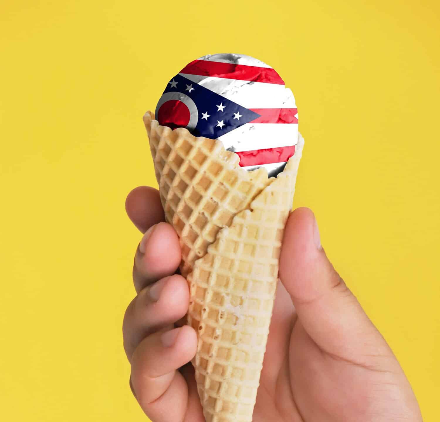 On a colorful background, a hand with ice cream in the form of the flag of State of Ohio