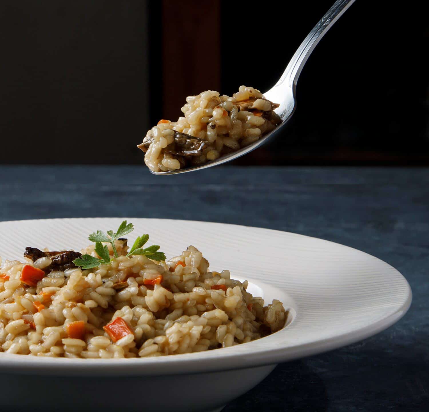 Risotto, Italian rice with mushrooms, vegetables and parsley served on white porcelain plate