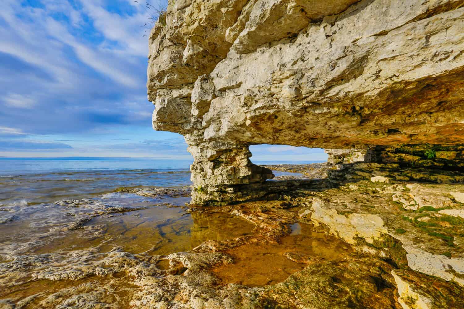 A rock arch window has been eroded by the waves at Door County, Wisconsin's Cave Point  with a cloudy blue sky.
