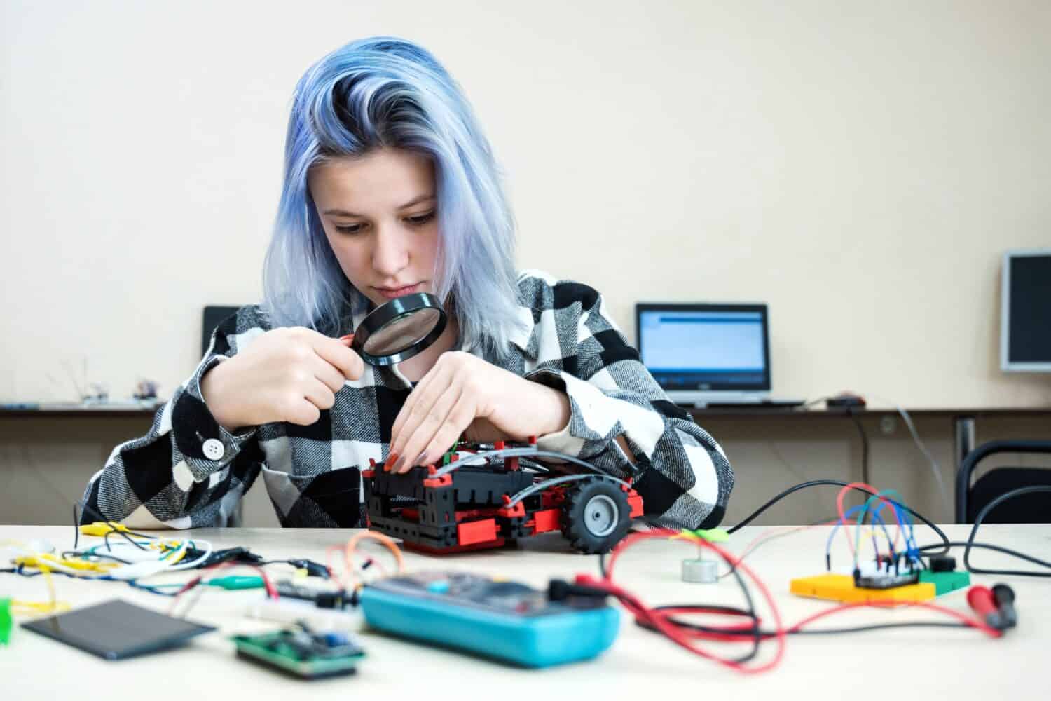 School students making robotic cars. Teenager girl at robotics school makes robot managed from the constructor, child learns robot constructing.
