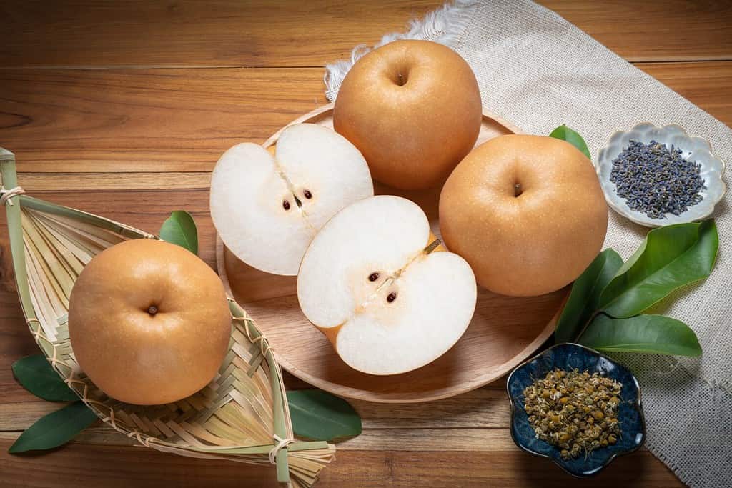 Premium Korean Sweet Pear with slice in wooden plate, Fresh Nashi pear or Korean pear fruit in wooden plate on wooden background.