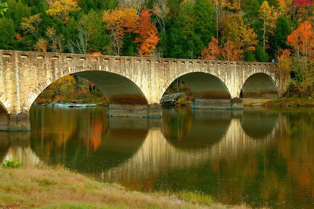 Fall colors surround a historic bridge, reflected in the Cumberland River just upstream of the Cumberland Falls in Kentucky, USA.