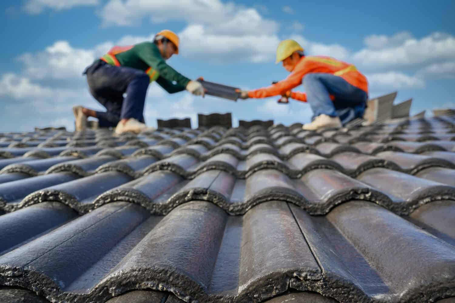 Select the focus on roof tiles. Blurred background of a roofer working on the roof of a house Use a drill to drill the screws to fix the cement tiles.