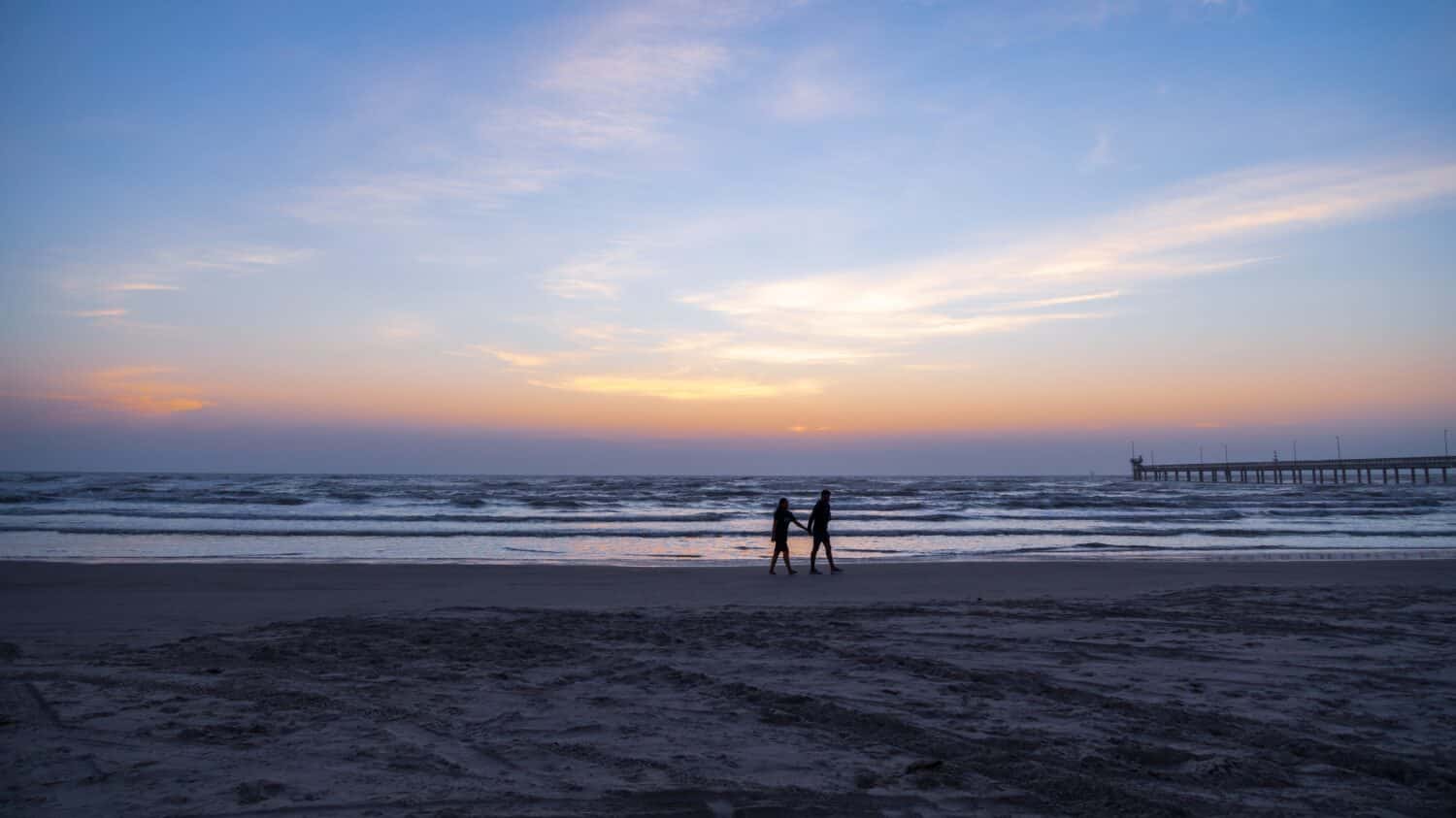 Silhouetted couple walking the beach at North Padre Island in the early morning just before sunrise 