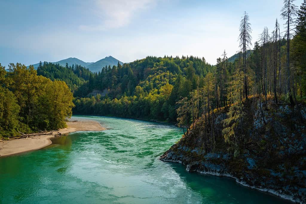 Panoramic landscape of turquoise-colored Skagit River water and green forest toward Glacier Peak over the Concrete Sauk Valley Bridge in Concrete, Washington State
