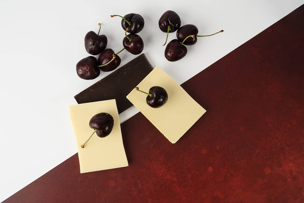 Flat lay of English Morello Cherries with white and dark chocolate on a mixed white and red background