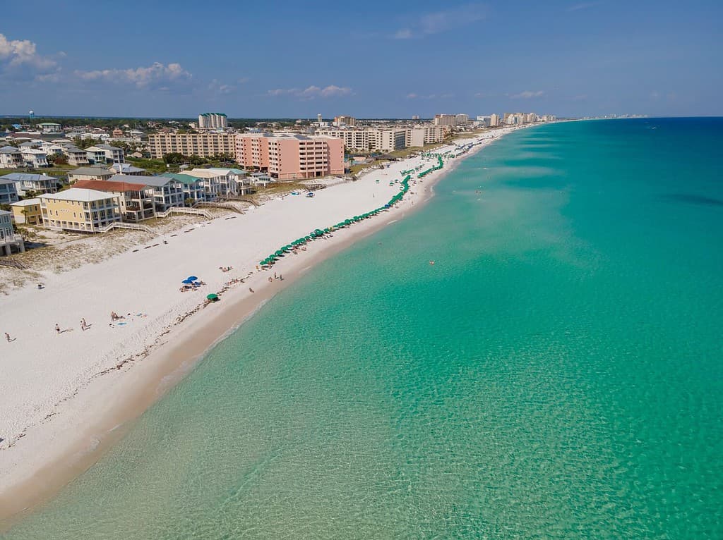 Beautiful aerial view of beach and ocean at East Jetty in Destin Florida. Scenic nature landscape with buildings and houses overlooking the sandy shore and clean water.