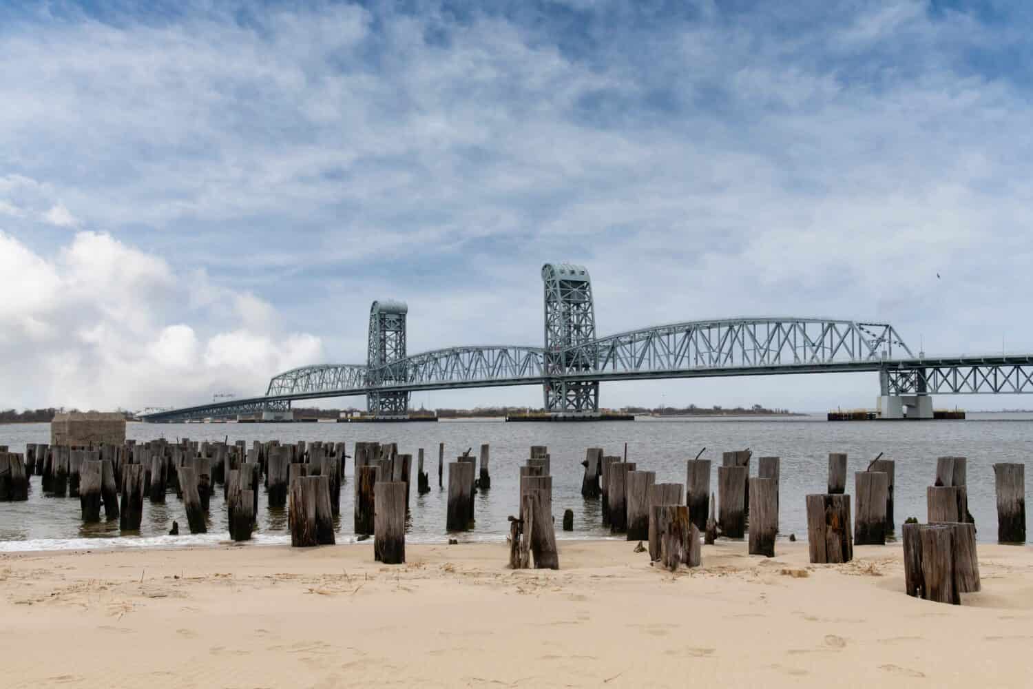 View from beach of Breezy Point, NY, USA, with remains of poles of pier towards vertical lift Marine Parkway–Gil Hodges Memorial Bridge (Marine Parkway Bridge crossing Rockaway Inlet 