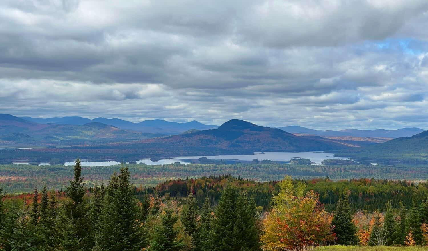 An aerial view of autumn trees near a lake and mountains in Jackman, Maine