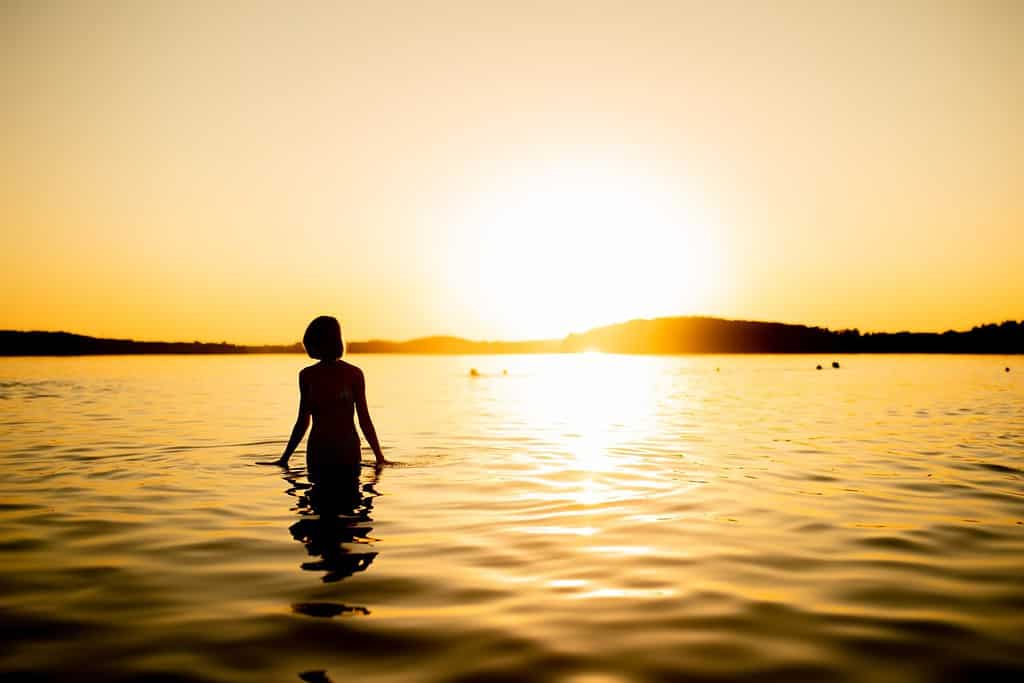 Silhouette of beautiful teenage girl having fun by a lake on warm and sunny summer evening. Pretty young girl on a sunset. Summer activities for families.
