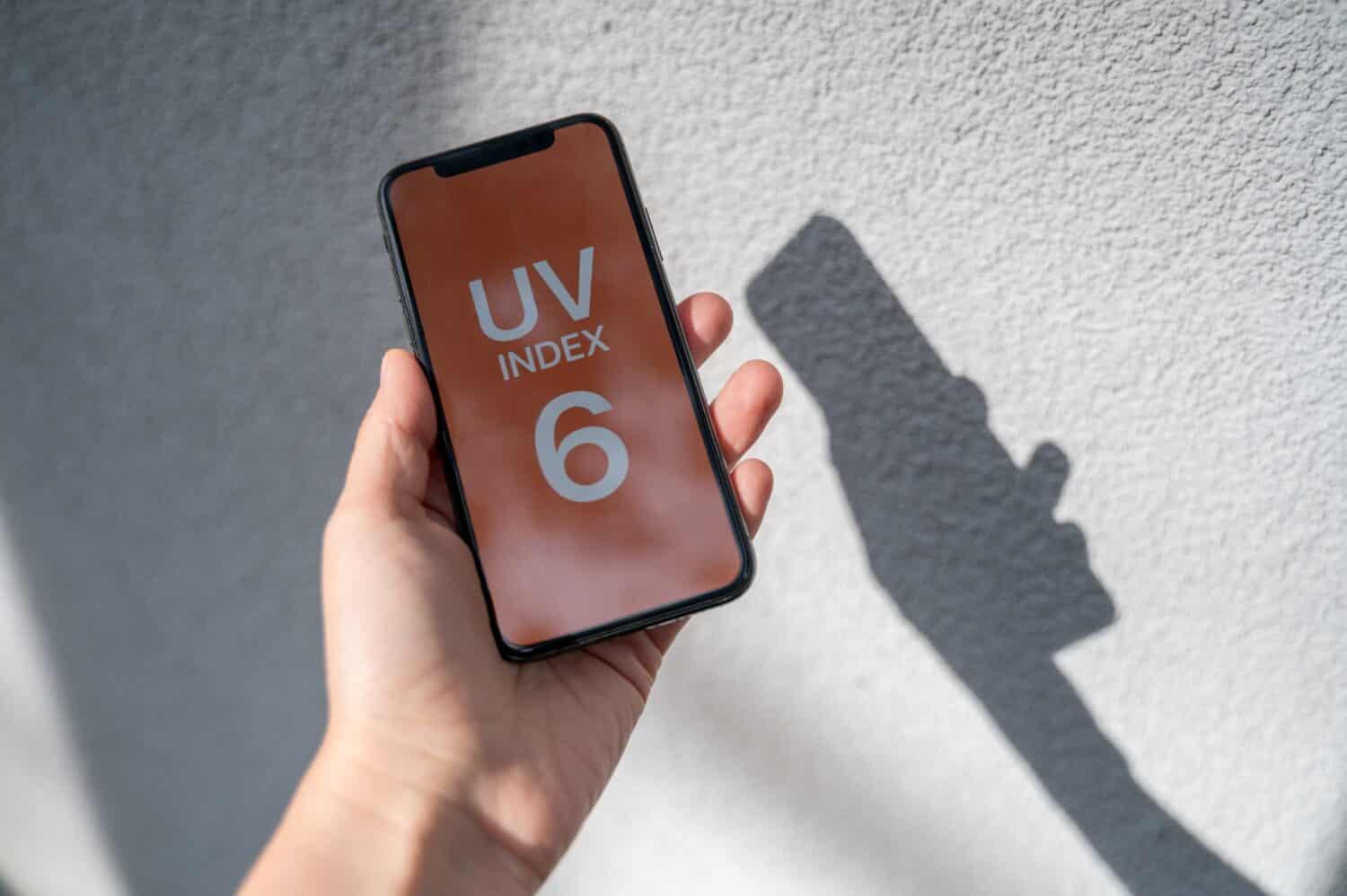 Smartphone in person hands with application showing UV index outside at sunny day