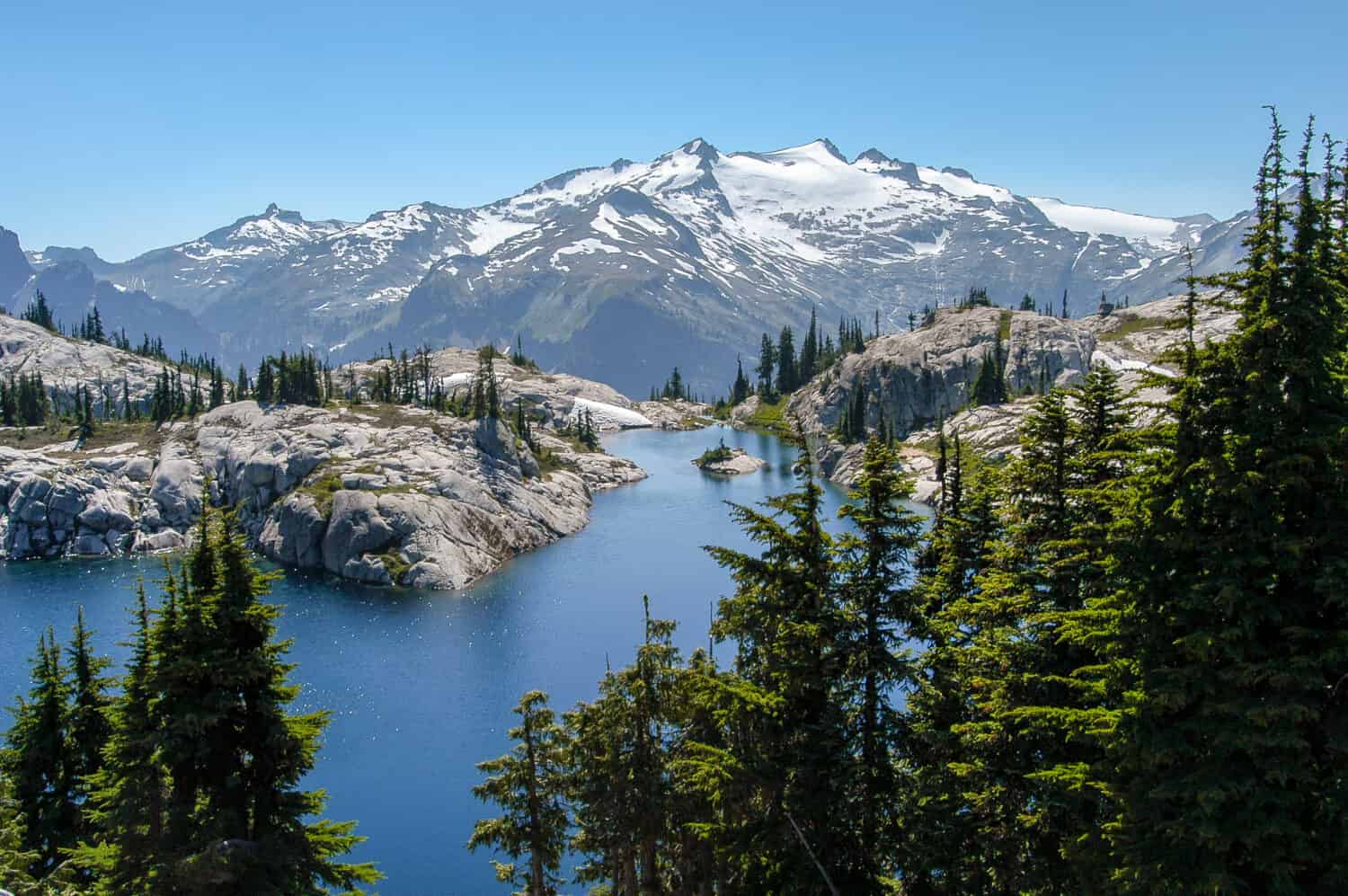 Picturesque sparkling Robin Lake surrounded by granite and trees with snow-capped Mt. Daniel towering in the background under a cloudless blue sky in the Alpine Lakes Wilderness, Washington State, USA