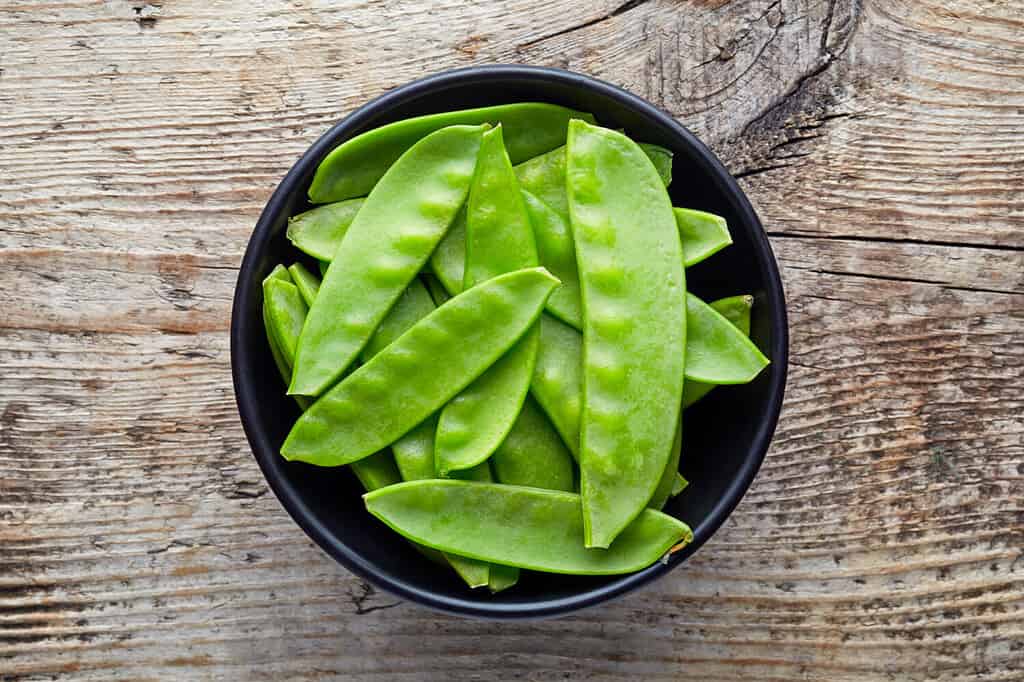 Bowl of snow peas on wooden background, top view