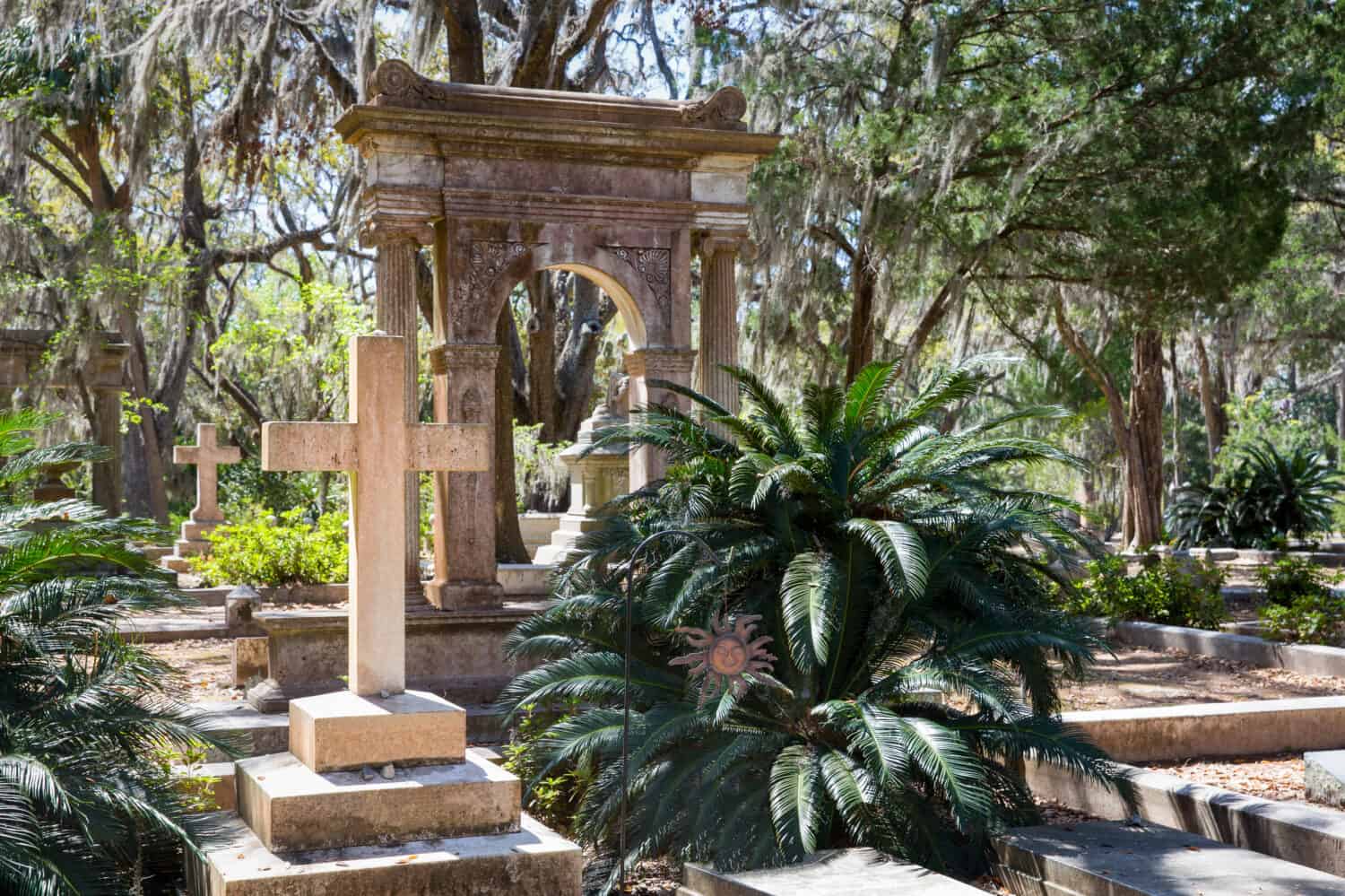 Historic Bonaventure Cemetery in Savannah, GA.  Serene scene with prominent cross in the foreground, lush vegetation, and Spanish moss.