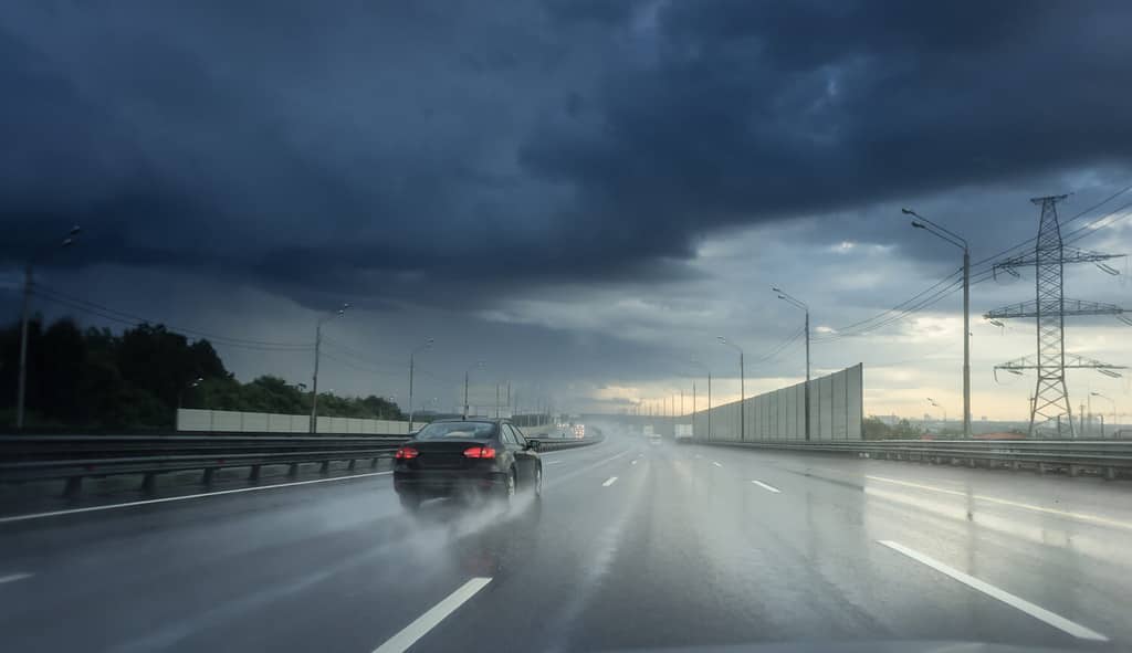 Drive car in rain on asphalt wet road. Clouds and sun.