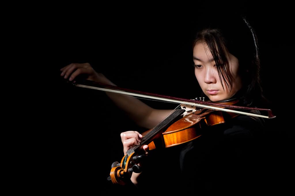 young woman playing violin on black background