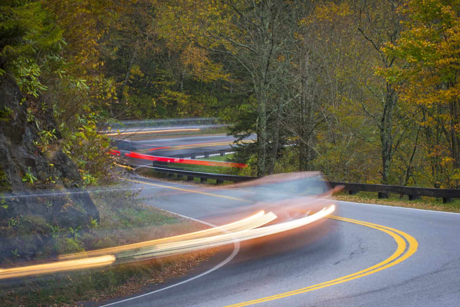 Twisting curvy road winding through fall colorful trees in national park with long exposure car streaks showing motion speed and transportation