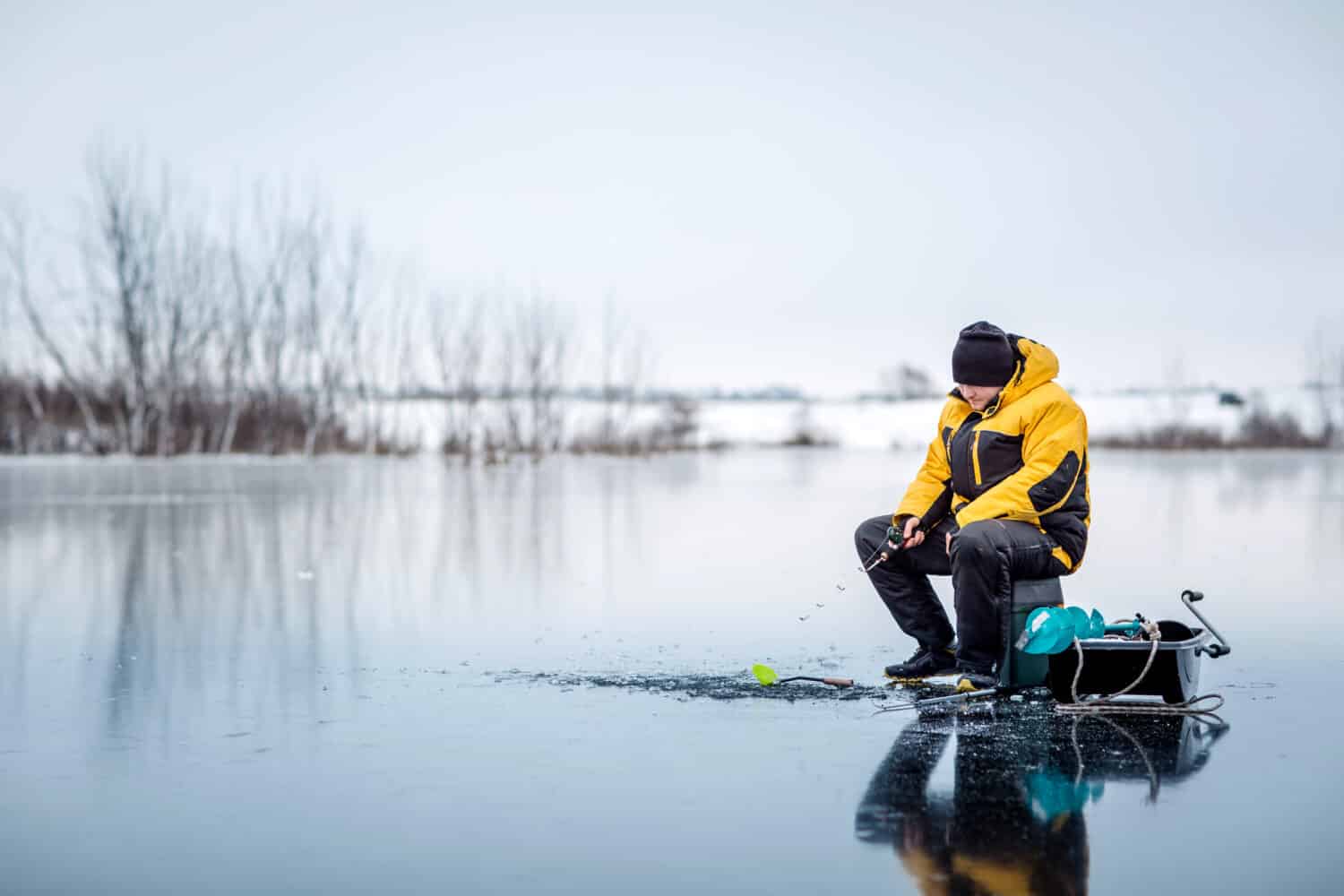 Man ice fishing on a frozen lake. winter holidays and people concept